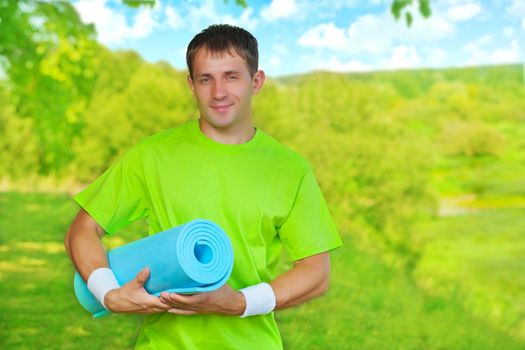a young sportsman standing on nature and holding yoga mat 