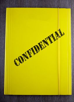 Yellow folder with black text "confidential" over wooden background