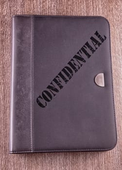 Gray folder over wooden background, with text "Confidential" over it