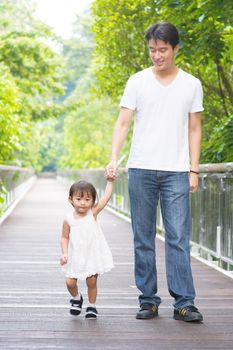 Happy Asian family outdoor activity. Father and daughter holding hands walking on garden path.