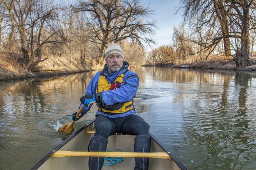senior canoe paddler in a  canoe on the Cache la Poudre River, Fort Collins, Colorado, winter or early spring, view from the bow