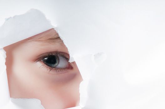 Child eye looking through a hole in a paper