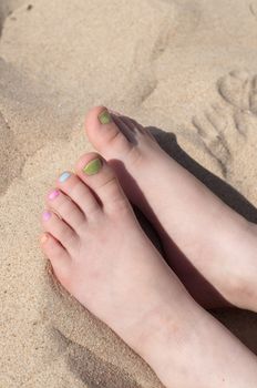 Baby fingers with multicolored pedicure on the sand