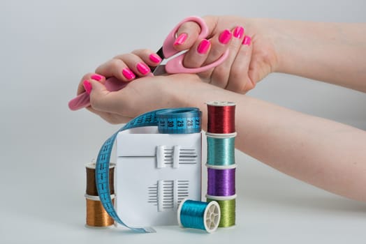 Coils with color strings of various color, sewing needles, scissors, sartorial centimeter and female hands bright manicure