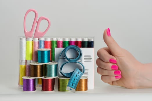 Coils with color strings of various color, sewing needles, scissors, sartorial centimeter and female hands bright manicure