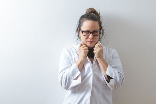 Woman doctor holding up her collar and leaning against a white wall