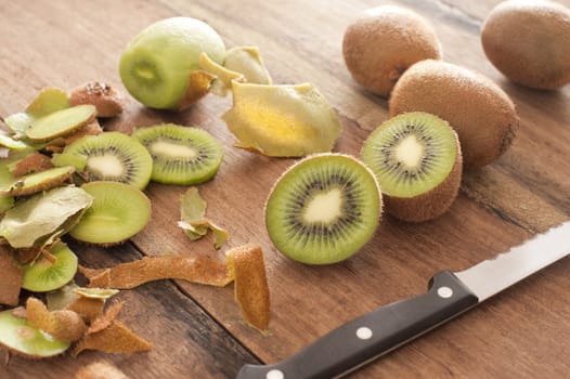 Closeup view of fresh kiwi fruit being prepared for dessert with a knife on a wooden kitchen counter