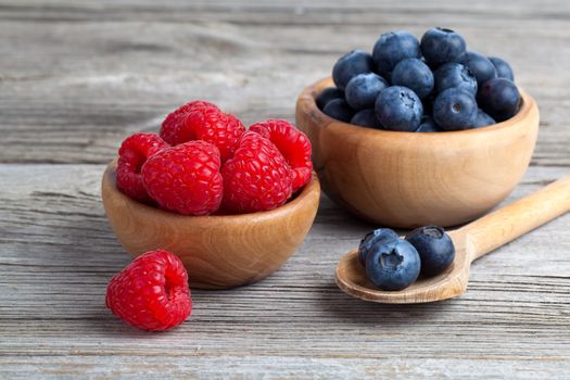 Blueberry and raspberries in bowls on wooden background