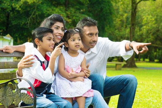 Happy Indian family at outdoor park. Candid portrait of parents and children having fun at garden park. Fingers pointing away.