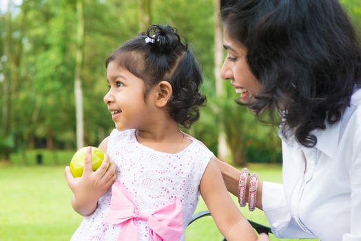 Happy Indian family. Asian girl holding an green apple at outdoor with mother.