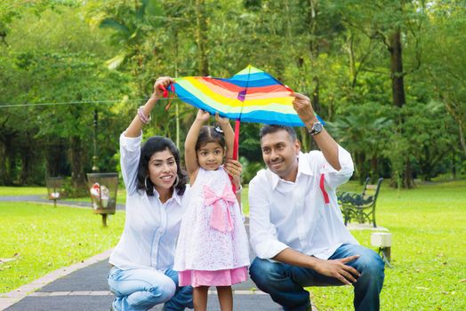 Indian family outdoor fun activity. Father and mother flying a colorful kite with daughter.