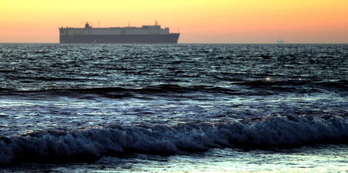 Sunset at a beach with cargo ship in the background.