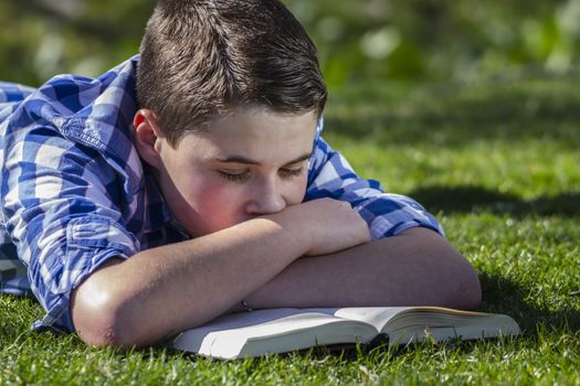 Young boy reading a book in the woods with shallow depth of field and copy space