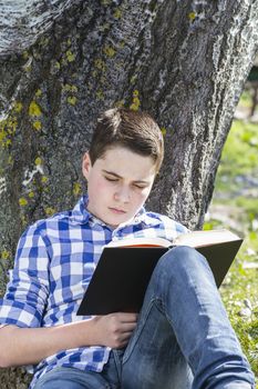 Young boy reading a book in the woods with shallow depth of field and copy space