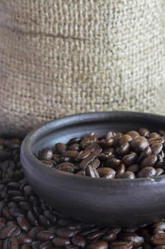 Coffee beans in a small clay pot. Image has a background of jute fibers