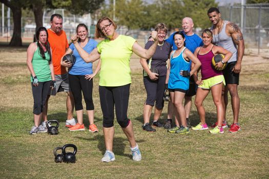 Confident mature woman flexing arms with fitness group standing