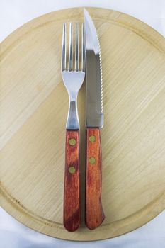 Fork and knife with red wooden handle on a plate of natural wood.