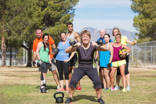 Smiling woman lifting kettle bell weights with group outdoors
