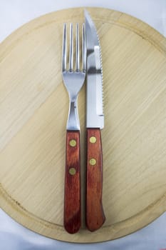 Fork and knife with red wooden handle on a plate of natural wood.