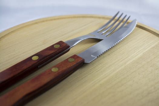 Fork and knife with red wooden handle on a plate of natural wood.