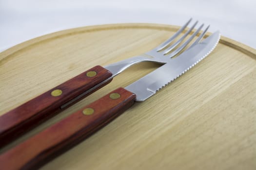 Fork and knife with red wooden handle on a plate of natural wood.