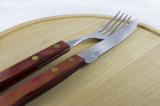 Fork and knife with red wooden handle on a plate of natural wood.