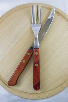 Fork and knife with red wooden handle on a plate of natural wood.