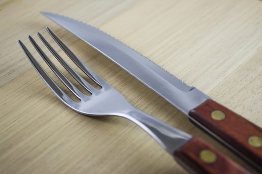 Fork and knife with red wooden handle on a plate of natural wood.