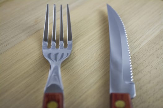 Fork and knife with red wooden handle on a plate of natural wood.