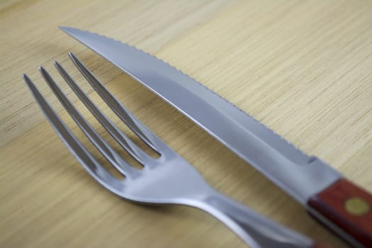 Fork and knife with red wooden handle on a plate of natural wood.