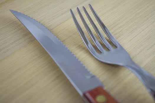 Fork and knife with red wooden handle on a plate of natural wood.