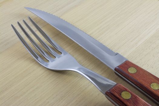 Fork and knife with red wooden handle on a plate of natural wood.