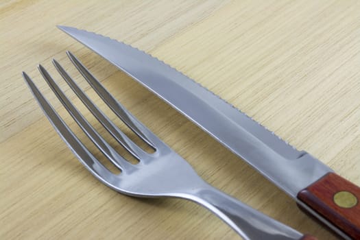 Fork and knife with red wooden handle on a plate of natural wood.