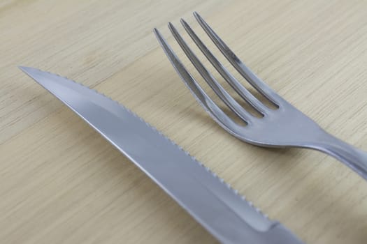 Fork and knife with red wooden handle on a plate of natural wood.