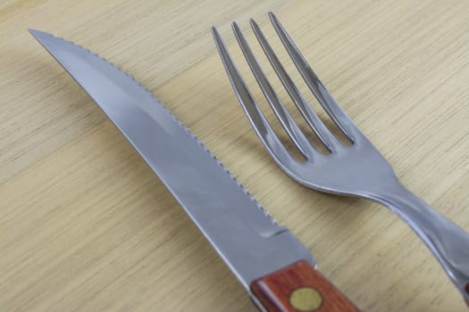 Fork and knife with red wooden handle on a plate of natural wood.