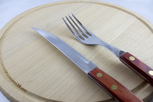 Fork and knife with red wooden handle on a plate of natural wood.
