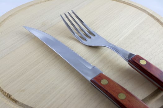 Fork and knife with red wooden handle on a plate of natural wood.