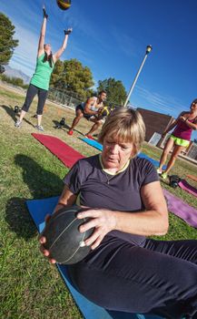 Mature woman doing sit-ups with medicine ball in fitness class