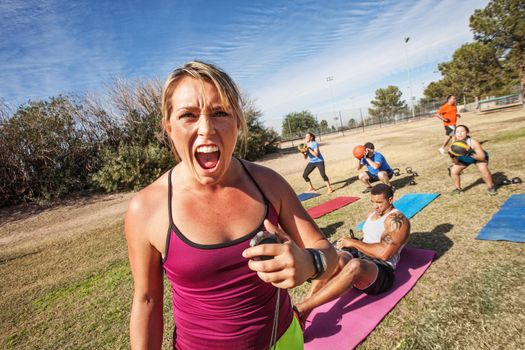 Intimidating boot camp fitness trainer with adult class outdoors