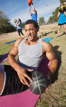Serious muscular man doing sit-ups with medicine ball outdoors