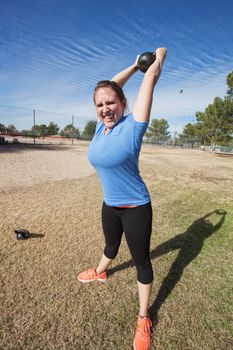 Enthusiastic Caucasian woman exercising with kettle bell weight outdoors