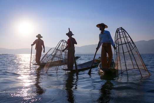Silhouette of traditional fishermans in wooden boat using a coop-like trap with net to catch fish in Inle lake, Myanmar