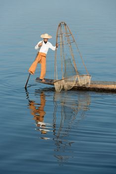 Traditional fisherman in wooden boat using a coop-like trap with net to catch fish in Inle lake, Myanmar