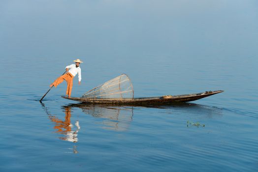 Traditional fisherman in wooden boat using a coop-like trap with net to catch fish in Inle lake, Myanmar