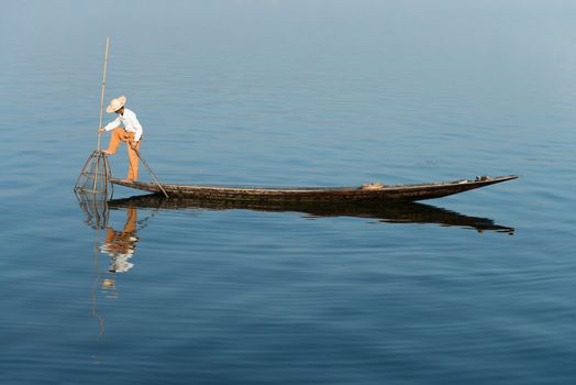 Traditional fisherman in wooden boat using a coop-like trap with net to catch fish in Inle lake, Myanmar