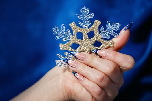 Female hand with beautiful manicure holding a snowflake shot closeup
