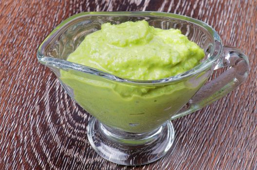 Hot Wasabi Sauce in Glass Gravy Boat isolated on Wooden background