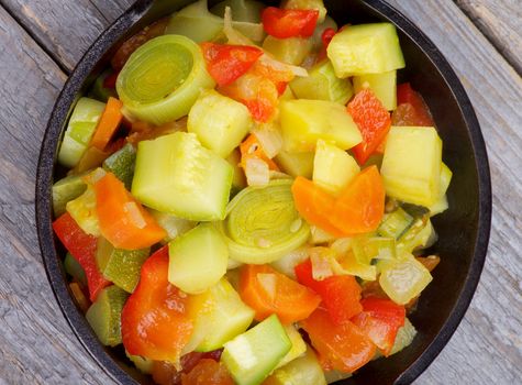 Vegetable Stew with Zucchini in Black Stew Pan closeup on Rustic Wooden background. Top View