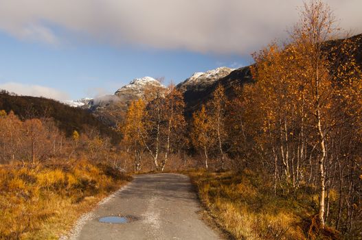 A beautiful mountian scenery in autumn, with a country road and a mountain peak covered in the seasons first snow