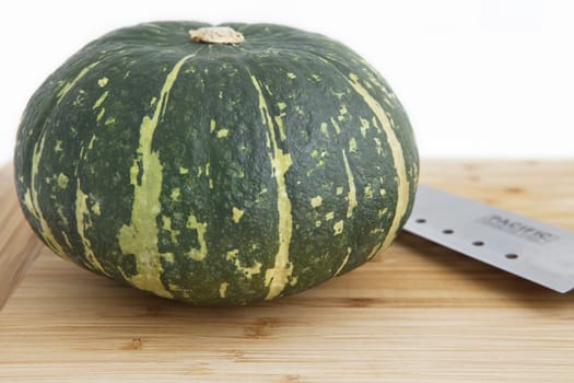 Close up of a farm fresh green pumpkin lying on a rustic wooden table with a sharp knife on display in a farmers market or ready for preparing a a healthy nutritious vegetable in a country kitchen